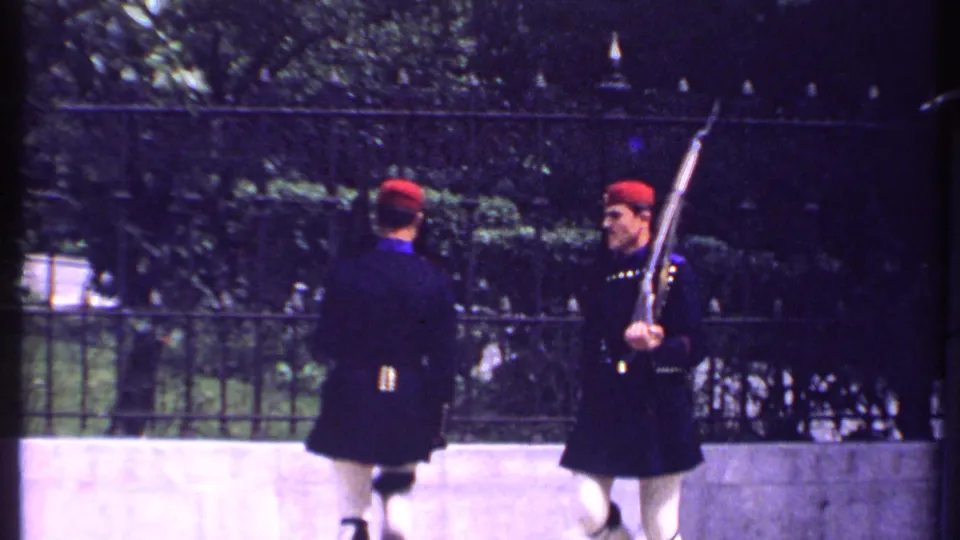 Kenya 1969 8mm frame of ceremonial guards in dark uniforms turning during a rifle drill beside a black iron fence.
