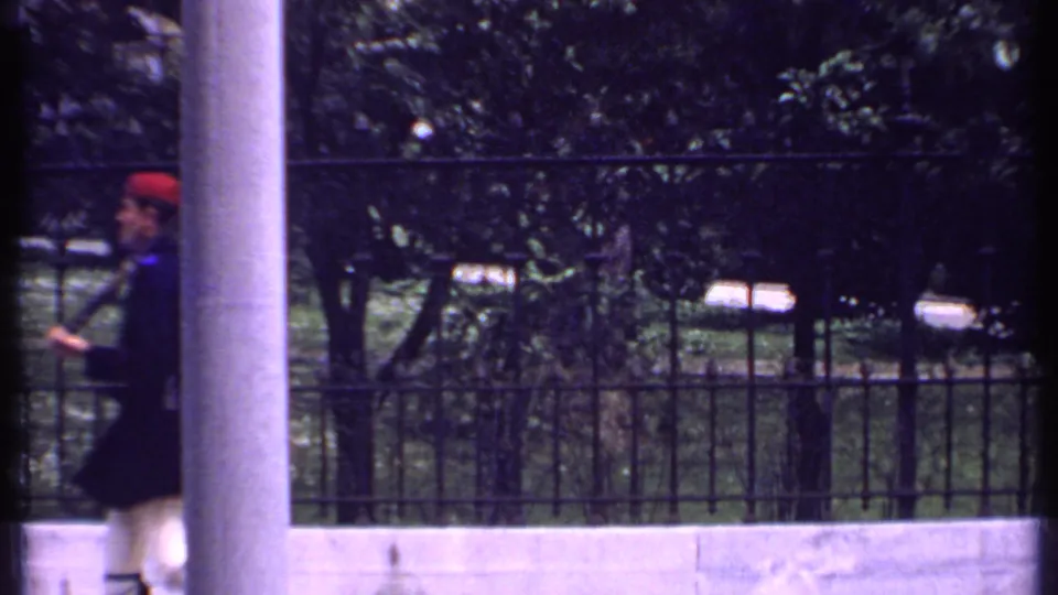 Uniformed soldiers in Kenya, 1969, appear mid-march with rifles, partly obscured by a vertical foreground post or film edge.
