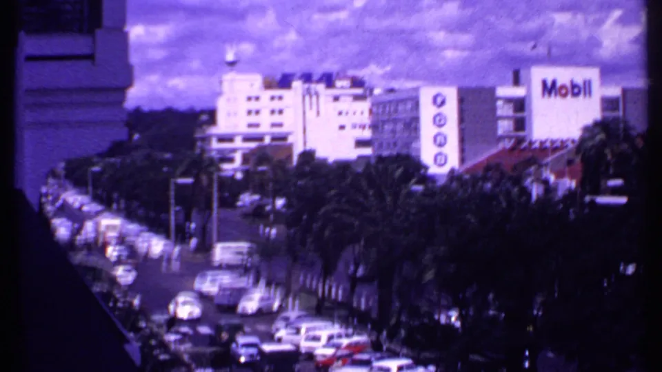 Elevated 1969 Kenya street view with classic cars, palms, mid-century buildings, and visible Mobil branding.