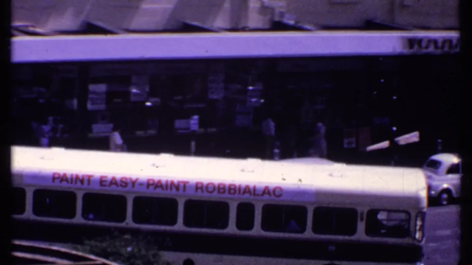 1969 Kenya street frame showing a white bus with red lettering near commercial frontage and partial vehicles.