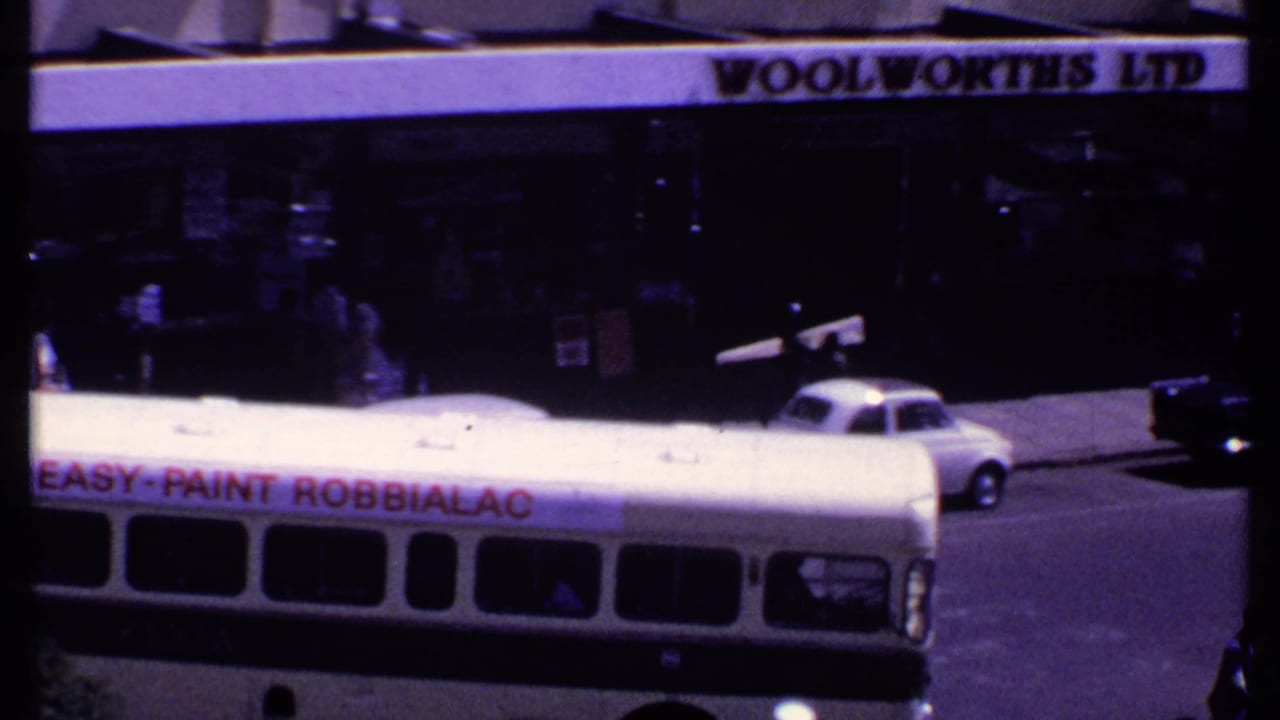 1969 Kenya street view with a white bus carrying a Robbialac paint advertisement beneath a Woolworths Ltd sign.