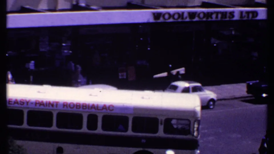 1969 Kenya street view with a white bus carrying a Robbialac paint advertisement beneath a Woolworths Ltd sign.