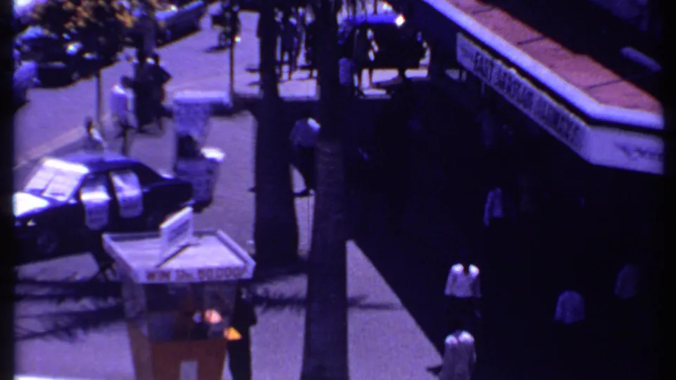 1969 Kenya home-movie view of pedestrians near a bus, car, newsstand, and palm-lined sidewalk.