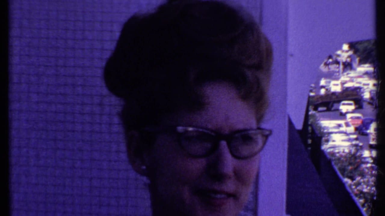 Close view of a woman with glasses beside a balcony, with street traffic visible at the edge.