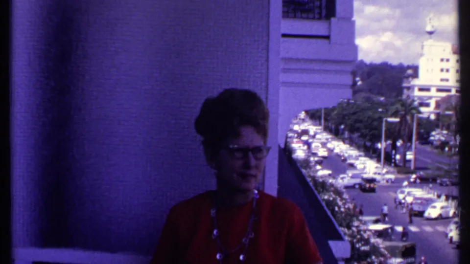 The 1969 Kenya balcony view shows the woman in red against a busy urban street with cars, palms, and a pale building in the distance.