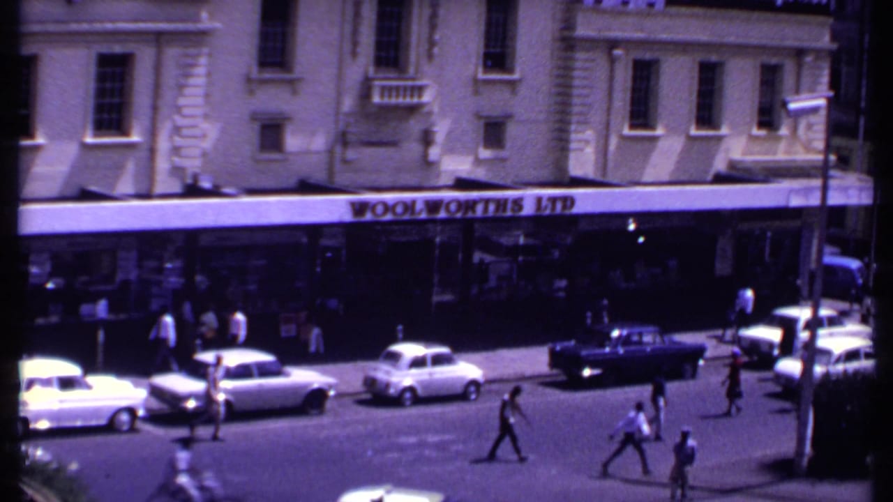 Wide street view outside a Woolworths Ltd storefront with cars and pedestrians.