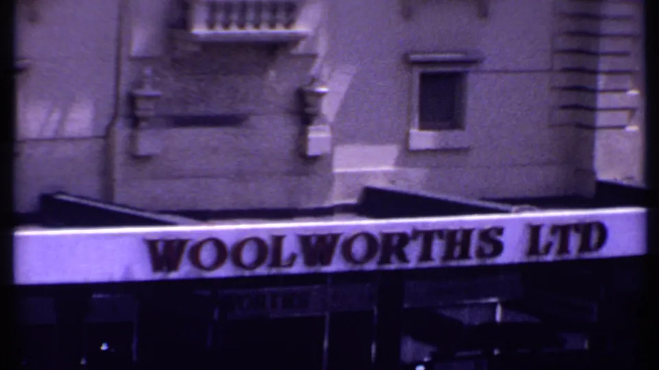 The final frame tightly crops the Woolworths Ltd entrance lettering, facade details, and shadowed storefront area in the 1969 Kenya street scene.