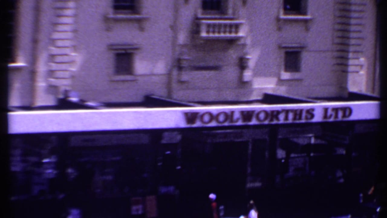 Busy street view with Woolworths LTD storefront, pedestrians, cars, and multi-story buildings.
