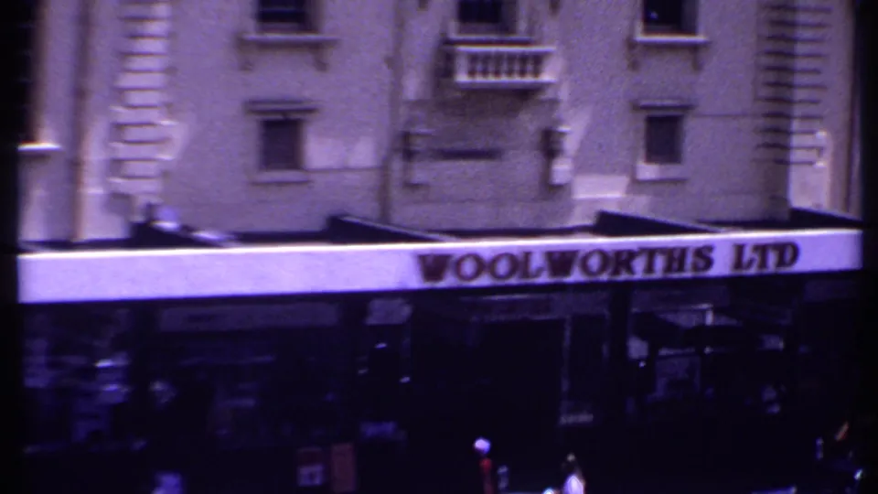 1969 Kenya 8mm street scene with a Woolworths LTD sign, pedestrians, period cars, and urban building facades.