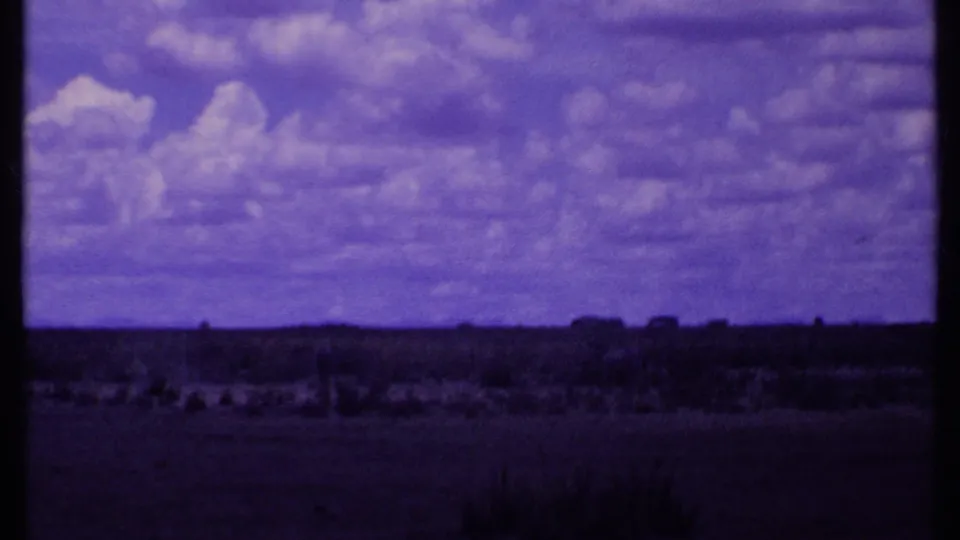 1969 Kenya 8mm frame showing dry grassland, a low horizon, scattered vegetation, and soft clouds with visible film grain.