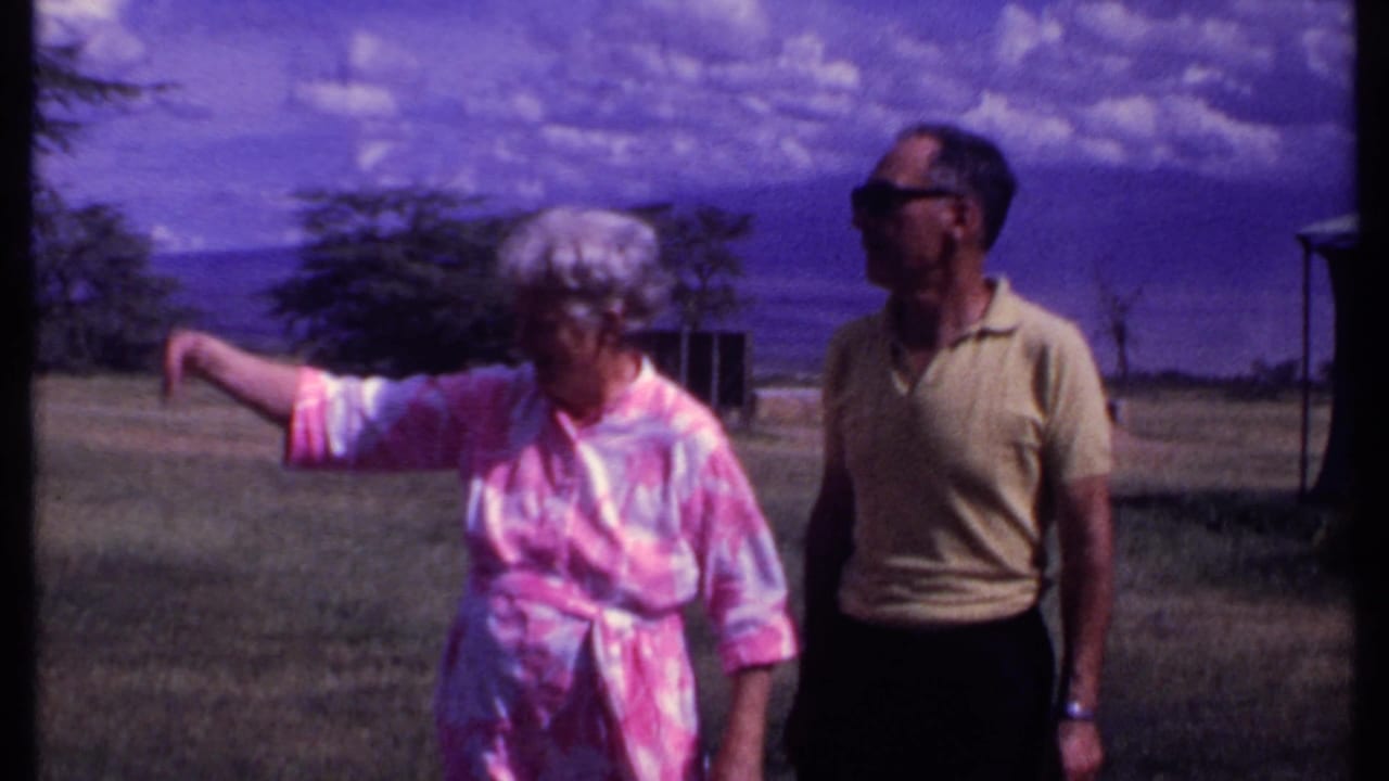 Older woman points across grass while an older man walks beside her outdoors.