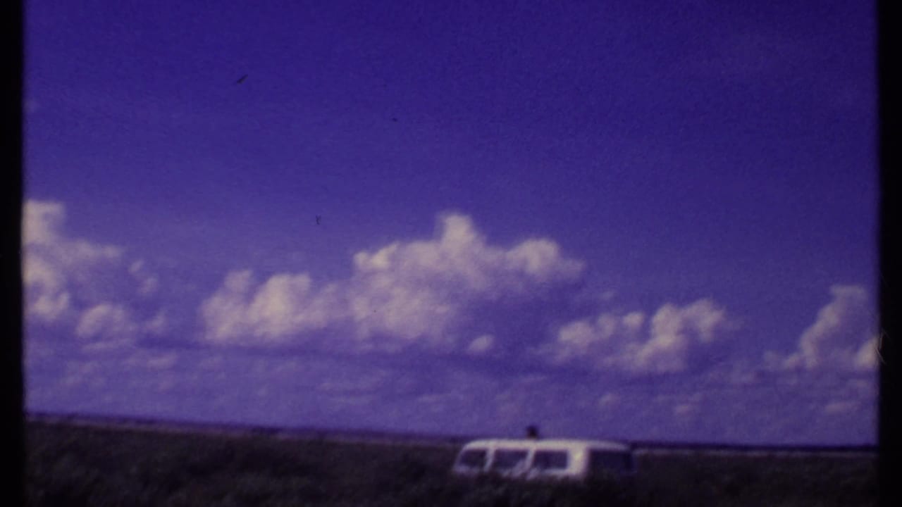 1969 Kenya safari view with a white van at the edge of the savanna under a wide sky with cumulus clouds.