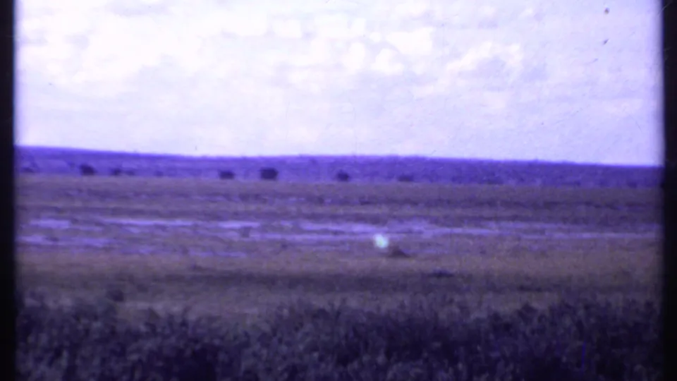 1969 Kenya 8mm frame showing open savanna, low hills, and distant wildlife beneath a partly cloudy sky.