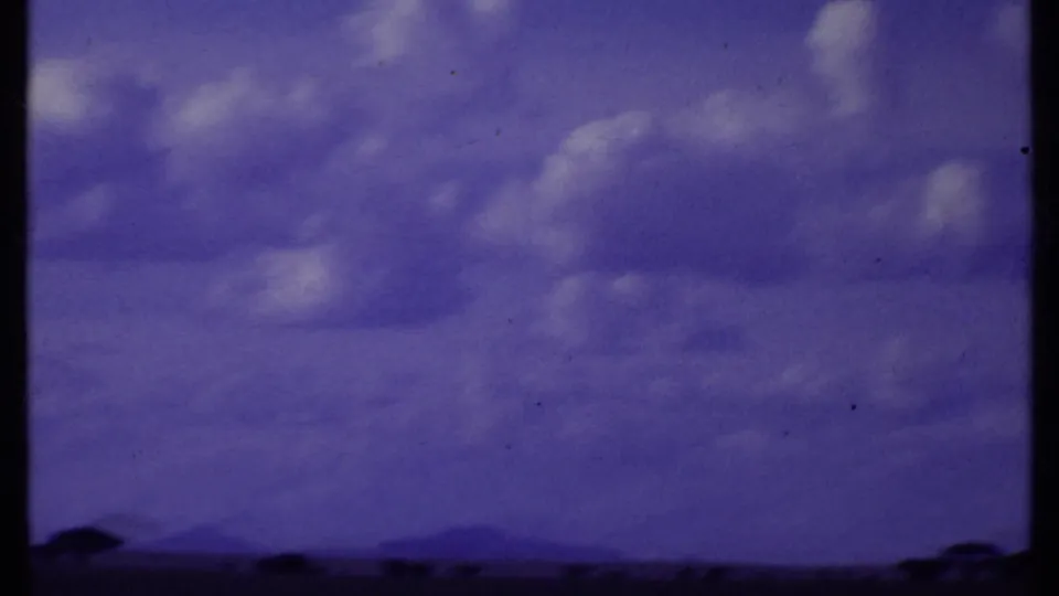Kenya 1969 8mm frame with soft clouds, distant low mountain shapes, and dark tree silhouettes along the savanna horizon.