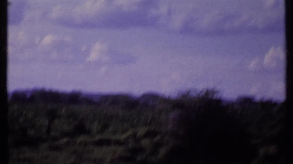 1969 Kenya 8mm frame showing a soft, distant savanna horizon with low vegetation, scattered trees, clouds, and dark film-frame borders.