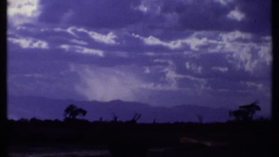1969 Kenya 8mm frame with broken clouds, distant hills, and sparse tree silhouettes across the savanna.