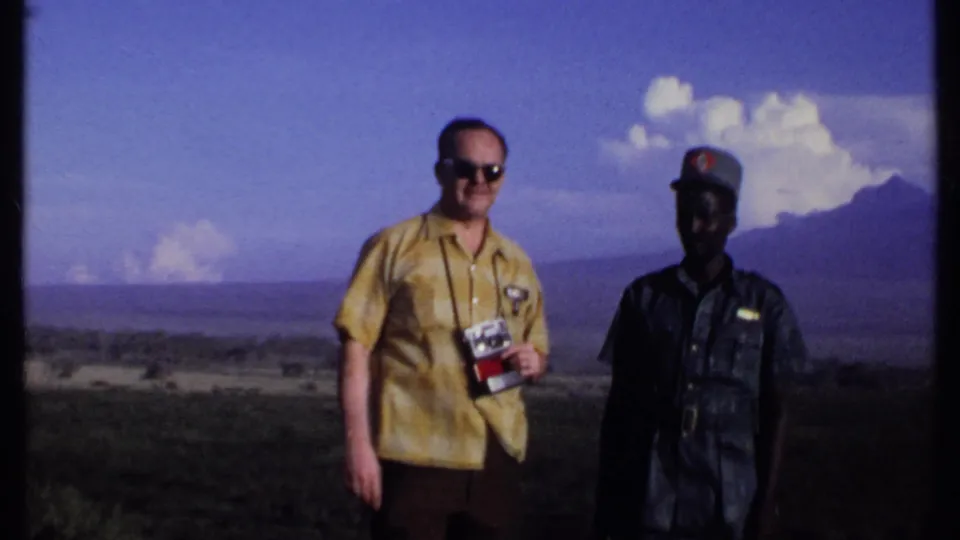 The 1969 Kenya frame shows a visitor holding a camera next to a uniformed man, with mountains and cloud formations in the distance.