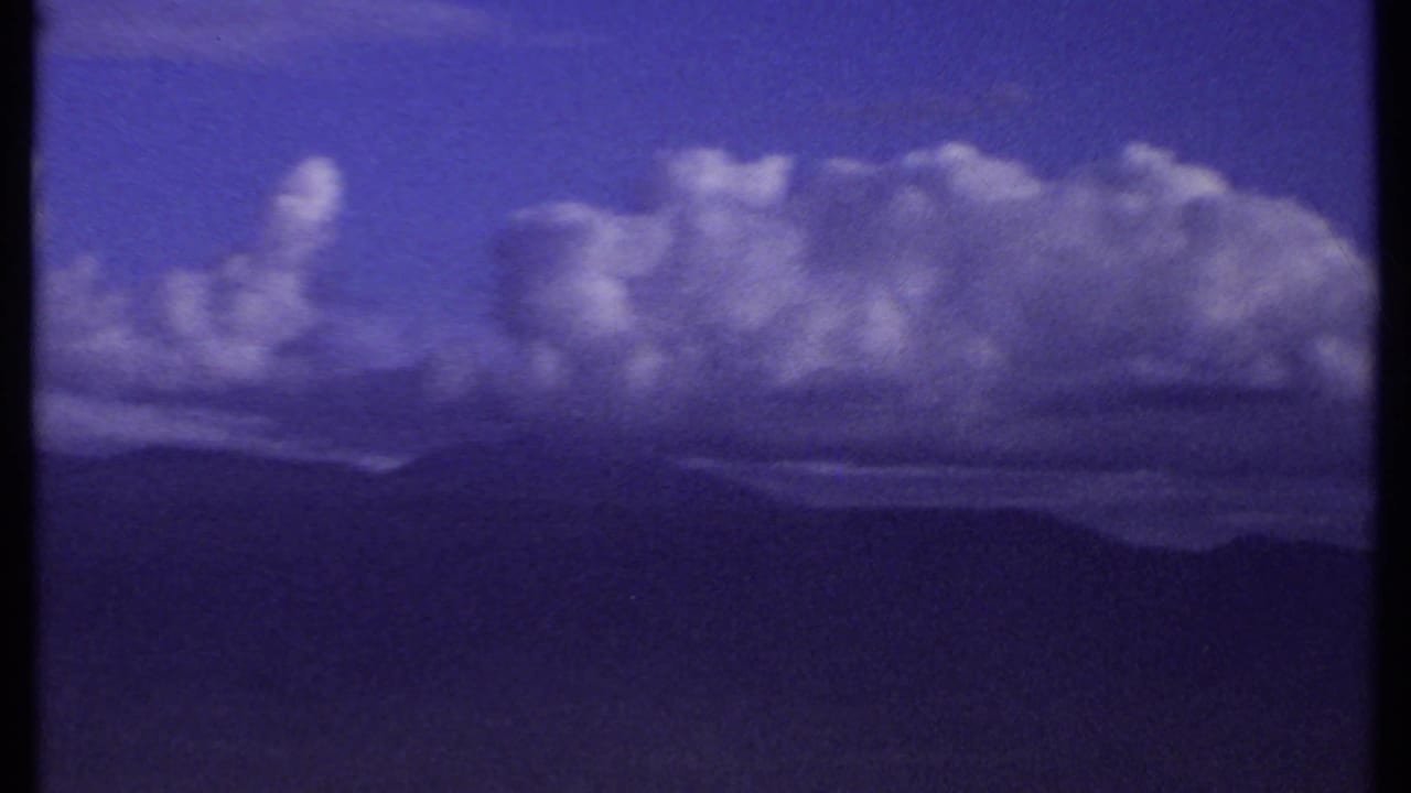 Blue sky with large clouds above dark distant mountain silhouettes.