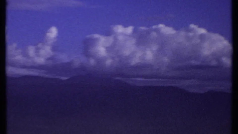 1969 Kenya 8mm frame showing billowing clouds over a hazy line of distant mountains under a deep blue sky.