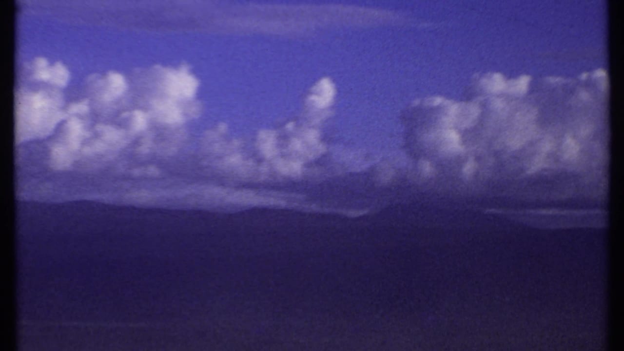 1969 Kenya 8mm frame with a broad cumulus cloud bank above layered, distant mountain silhouettes.