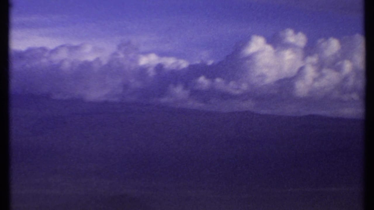 1969 Kenya 8mm frame with towering clouds across a distant mountain skyline and a cool purple-blue film cast.
