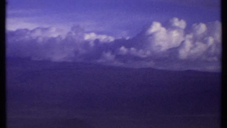 1969 Kenya 8mm frame with towering clouds across a distant mountain skyline and a cool purple-blue film cast.