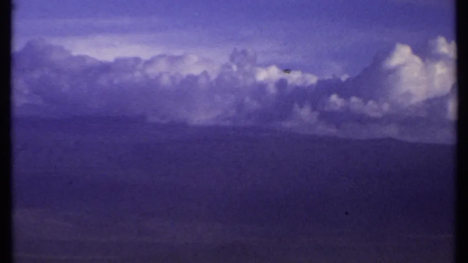 1969 Kenya 8mm frame showing a dark layered cloud formation under a violet-blue sky, with no people or structures visible.