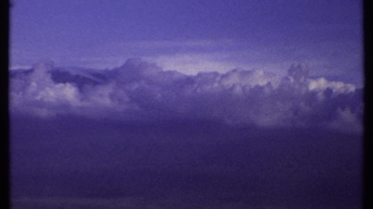 1969 Kenya 8mm frame with a broad cloud formation stretching across a dim horizon, rendered with strong purple-blue film color shift.