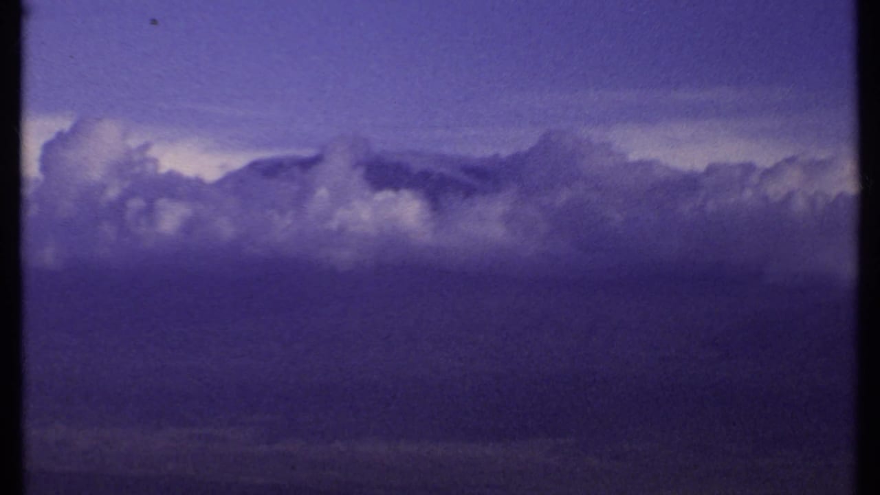 1969 Kenya 8mm frame showing billowing clouds against a darkened purple-blue sky during a slow pan across the weather system.