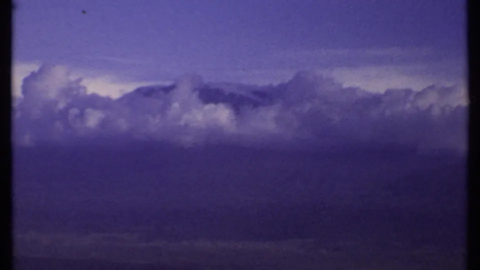 1969 Kenya 8mm frame showing billowing clouds against a darkened purple-blue sky during a slow pan across the weather system.