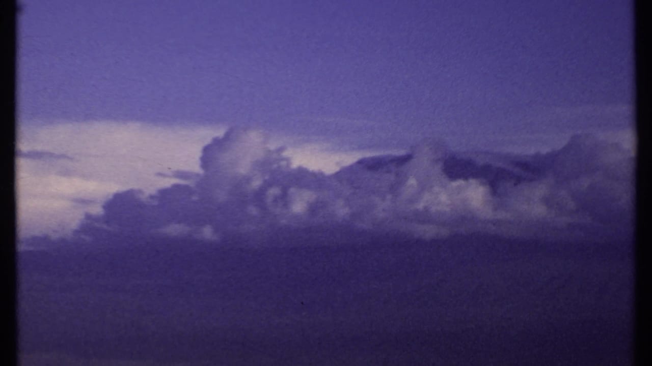 1969 Kenya 8mm frame showing a cloud mass beside a pale horizon opening, with purple-blue color shift and no identifiable landmarks.