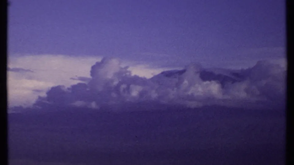 1969 Kenya 8mm frame showing a cloud mass beside a pale horizon opening, with purple-blue color shift and no identifiable landmarks.