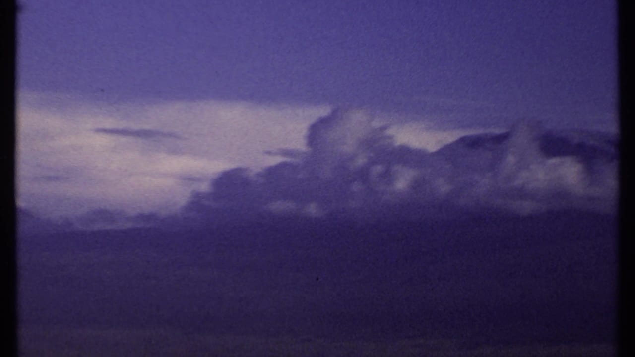 Dark mountain ridge beneath a purple sky with layered storm clouds.