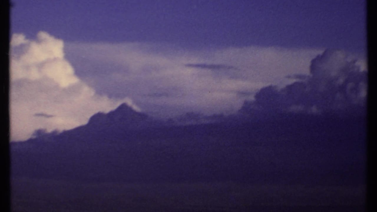 1969 Kenya 8mm frame with a peaked mountain silhouette, dark cloud cover, and a bright vertical cloud mass above the ridge.