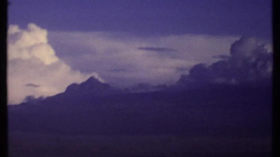 1969 Kenya 8mm frame with a peaked mountain silhouette, dark cloud cover, and a bright vertical cloud mass above the ridge.