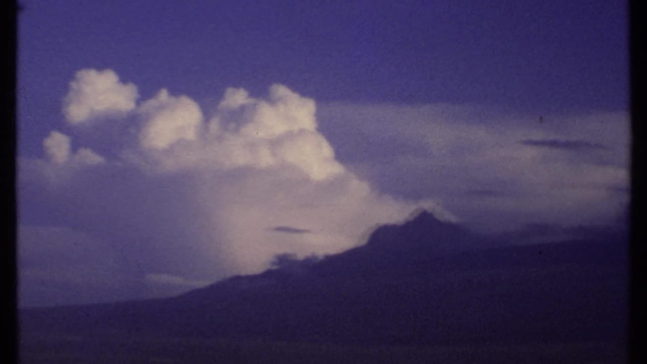 1969 Kenya 8mm frame showing a towering white storm cloud above a dark distant ridge, with saturated sky and soft home-movie texture.