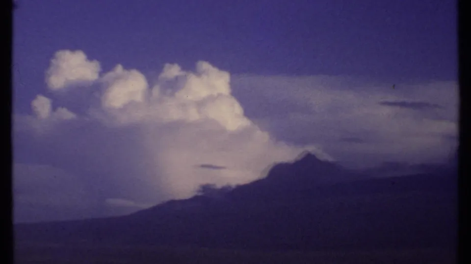 1969 Kenya 8mm frame showing a towering white storm cloud above a dark distant ridge, with saturated sky and soft home-movie texture.