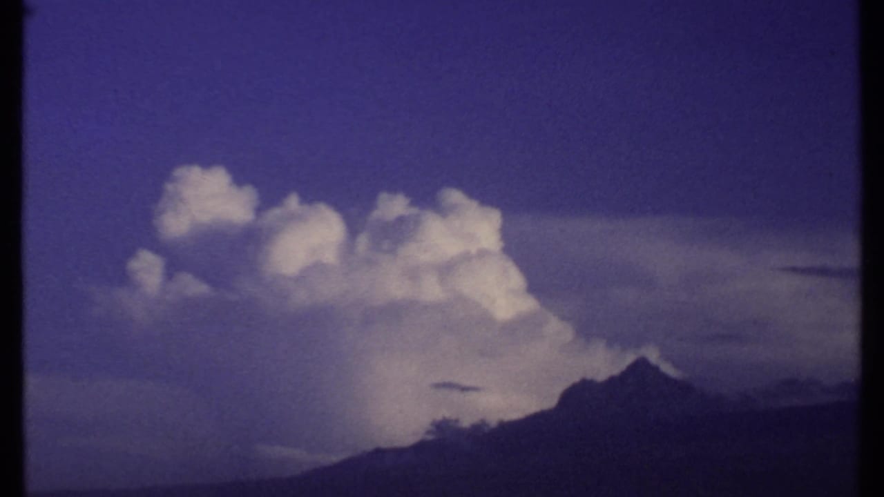 1969 Kenya 8mm frame with a large white cloud formation, a dark mountain peak, and a moody saturated sky.