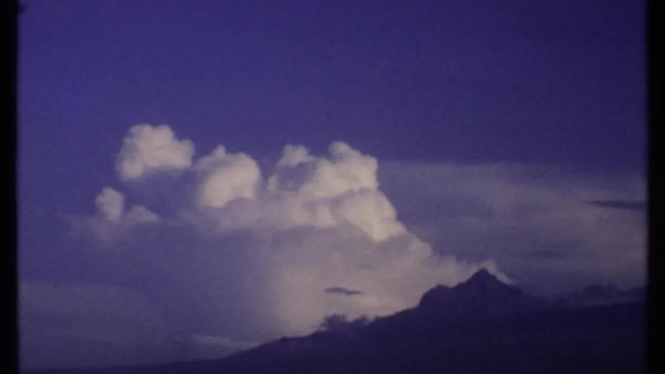 1969 Kenya 8mm frame with a large white cloud formation, a dark mountain peak, and a moody saturated sky.