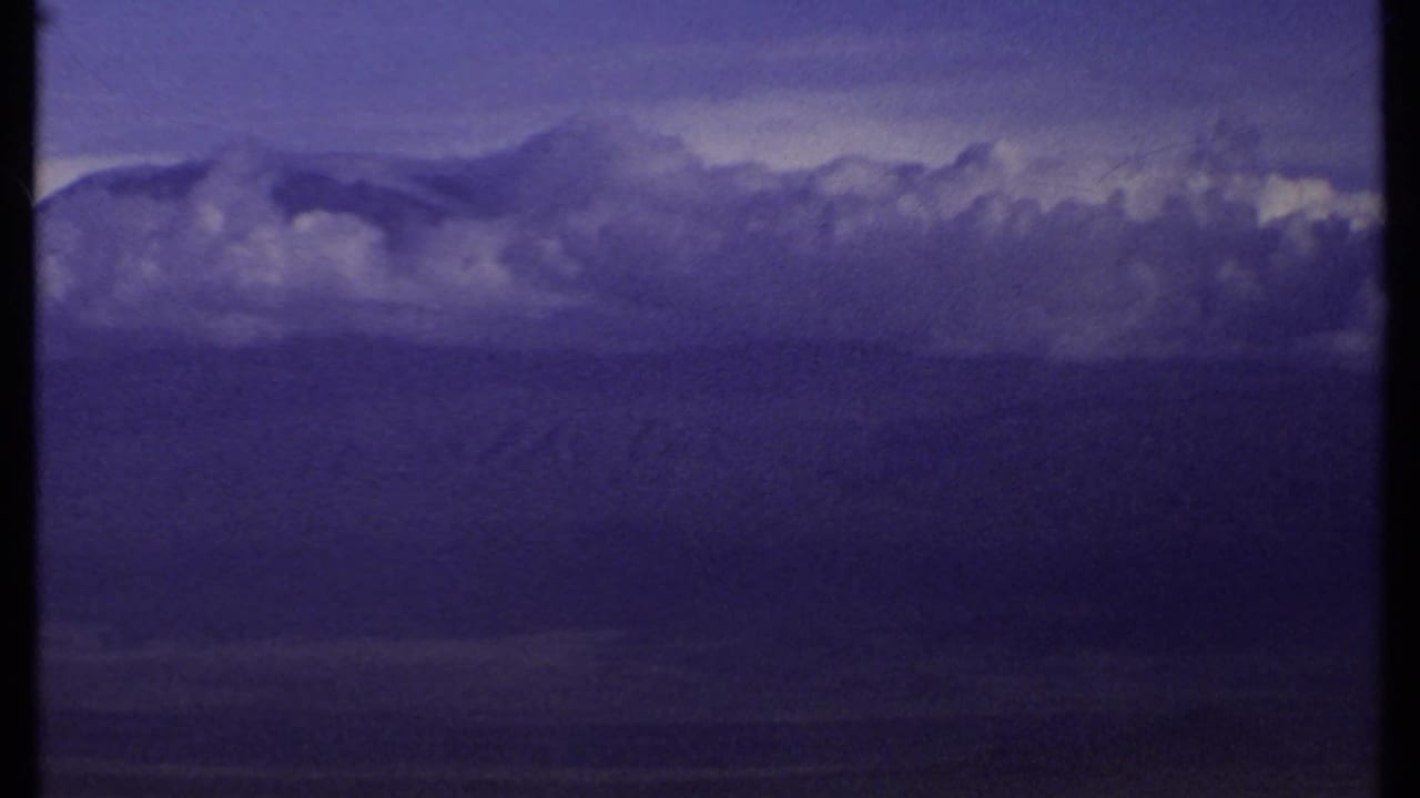 Purple-hued clouds and distant landscape seen from a hillside.