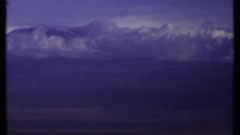1969 Kenya 8mm frame showing a broad distant landscape under heavy purple-blue clouds, with no people clearly visible in this frame.