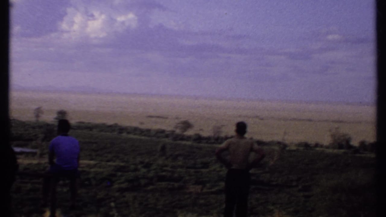Two people stand on a hillside looking across a broad plain.