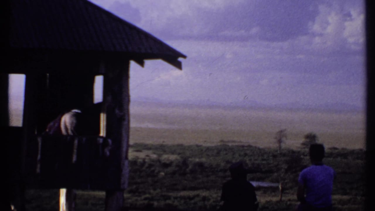 1969 Kenya 8mm frame showing tourists by a rustic lookout shelter facing a broad hazy plain.