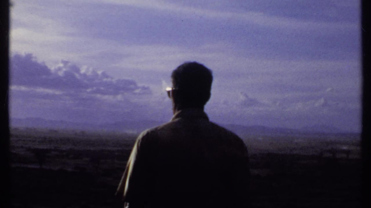 In 1969 Kenya footage, a man in dark sunglasses stands in silhouette with his back partly to the camera, looking over open terrain.