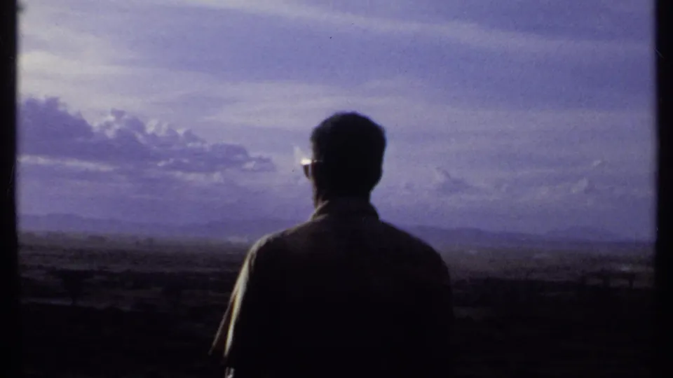 In 1969 Kenya footage, a man in dark sunglasses stands in silhouette with his back partly to the camera, looking over open terrain.