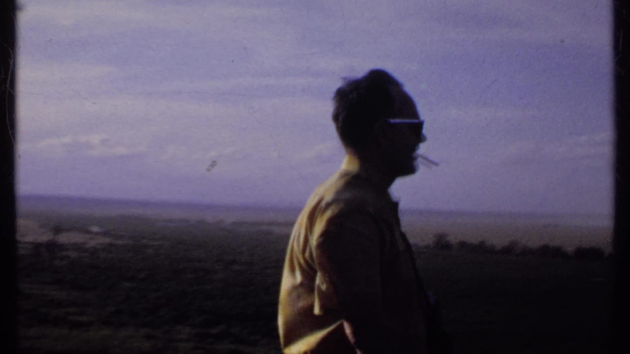 A side view shows the man with sunglasses and a cigarette, his shirt catching light as he faces across the Kenya landscape.