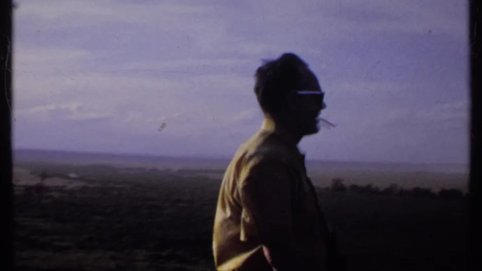 A side view shows the man with sunglasses and a cigarette, his shirt catching light as he faces across the Kenya landscape.