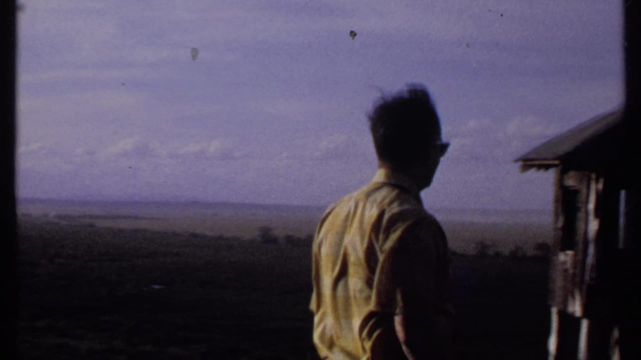 Man in yellow shirt stands beside a small structure overlooking a wide landscape.