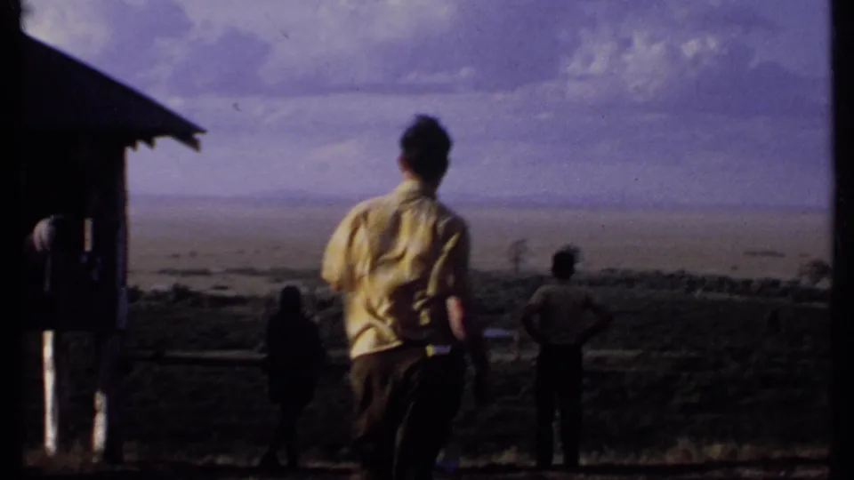 Several people in 1969 Kenya footage stand near a wooden rail at an elevated viewpoint, facing the open countryside.