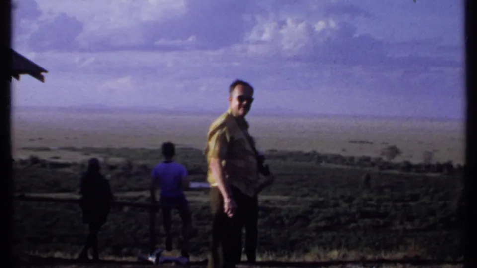 In Kenya 1969 footage, a man in sunglasses turns back toward the camera while others continue facing the distant view.